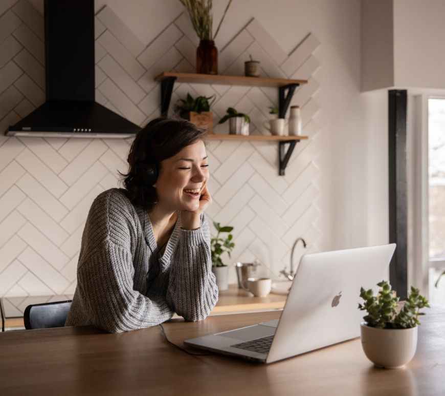 smiling woman talking via laptop in kitchen