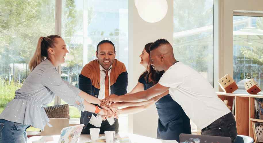 smiling multiracial coworkers with hands together in office